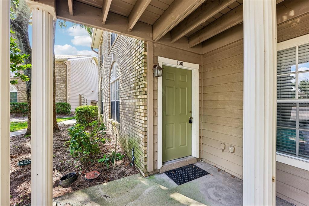 A covered entryway features a green front door numbered 100, brick siding, and white columns — 124 RESERVE CIRCLE UNIT 100, OVIEDO, FL