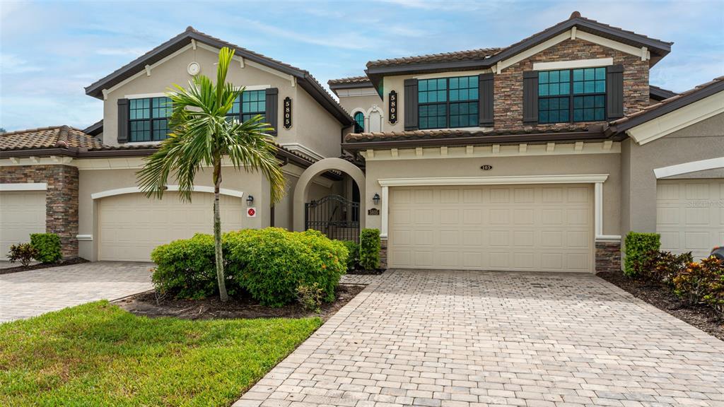 A two-story house exterior features a paved driveway, a palm tree, and multiple garage doors — 5805 WAKE FOREST RUN UNIT 103, LAKEWOOD RANCH, FL