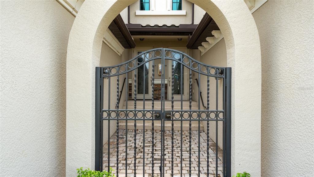 A black metal gate stands in front of a stone-paved entryway leading to double doors — 5805 WAKE FOREST RUN UNIT 103, LAKEWOOD RANCH, FL