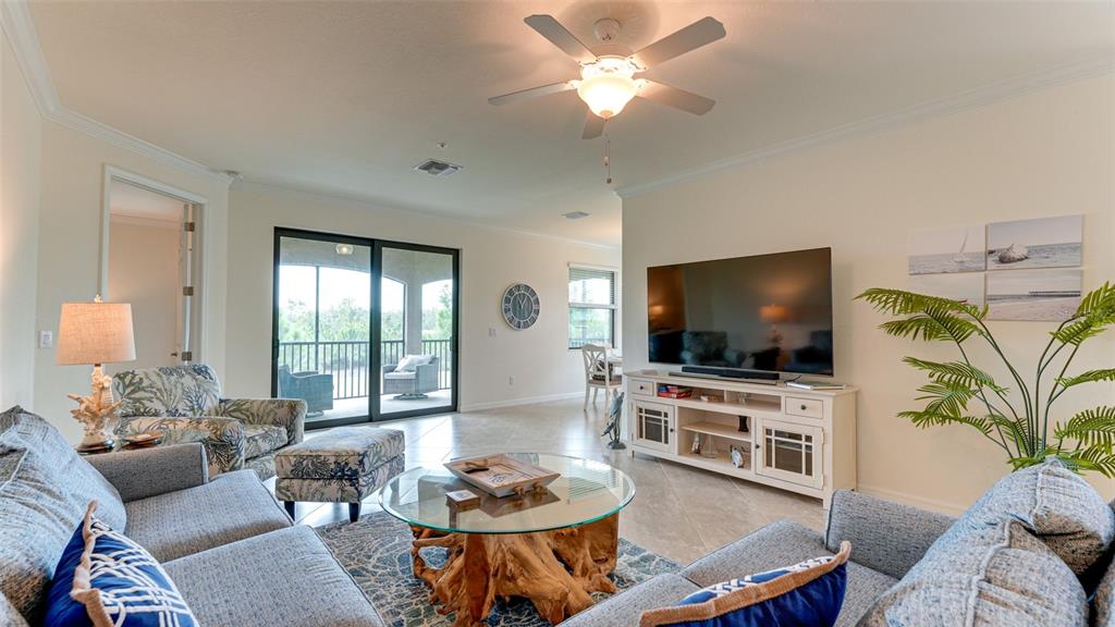 A living room features a glass-topped driftwood coffee table, a television console, and sliding doors — 5805 WAKE FOREST RUN UNIT 103, LAKEWOOD RANCH, FL
