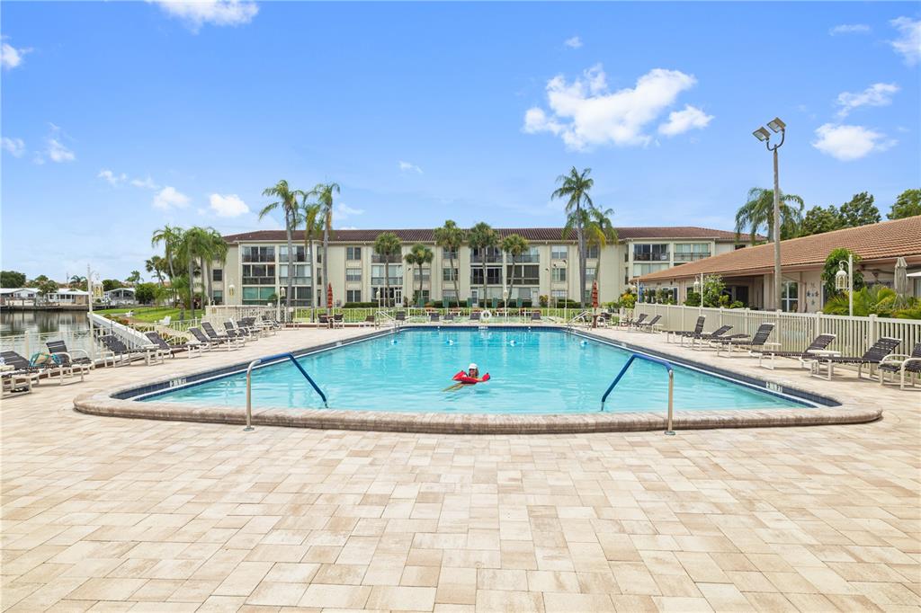 A swimming pool sits on a paved patio in front of a multi-story apartment building — 19029 US HIGHWAY 19 N UNIT 3-1, CLEARWATER, FL