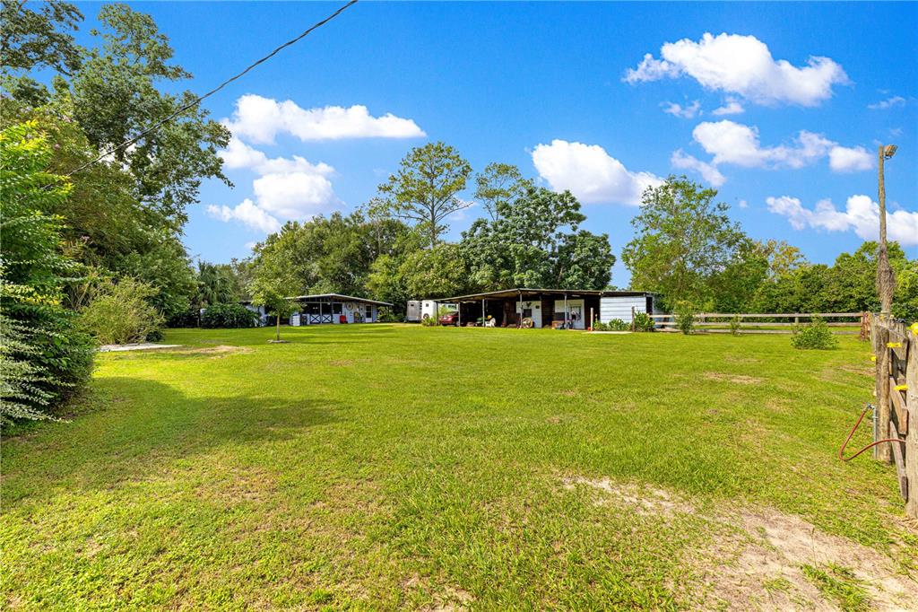 A large grassy yard features two detached outbuildings under a bright blue sky — 8221 SE 126TH PLACE, BELLEVIEW, FL