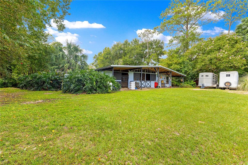 A white horse barn with a covered porch sits on a grassy lot with trailers — 8221 SE 126TH PLACE, BELLEVIEW, FL