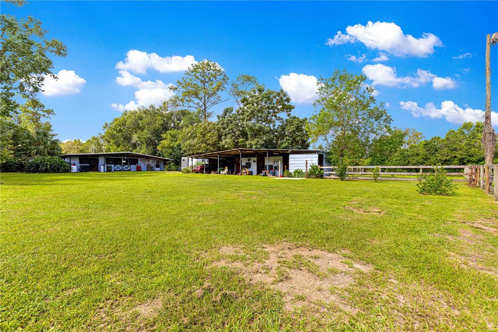 A large grassy field leads to a long, single-story barn structure under a blue sky — 8221 SE 126TH PLACE, BELLEVIEW, FL