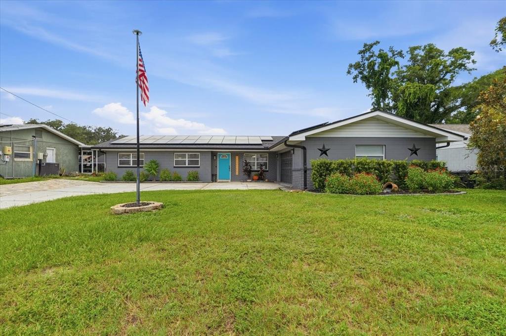A single-story gray house with a teal front door, solar panels, and an American flag — 121 LOWELL ROAD, WINTER HAVEN, FL