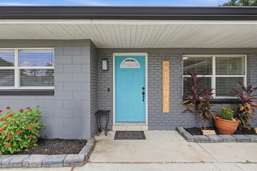 A gray concrete block house exterior features a bright blue front door and a welcome sign — 121 LOWELL ROAD, WINTER HAVEN, FL