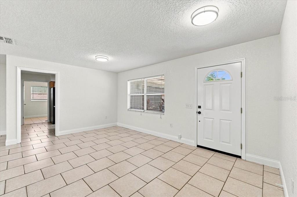A bright, empty room with white walls, tile flooring, a front door, and a window — 121 LOWELL ROAD, WINTER HAVEN, FL