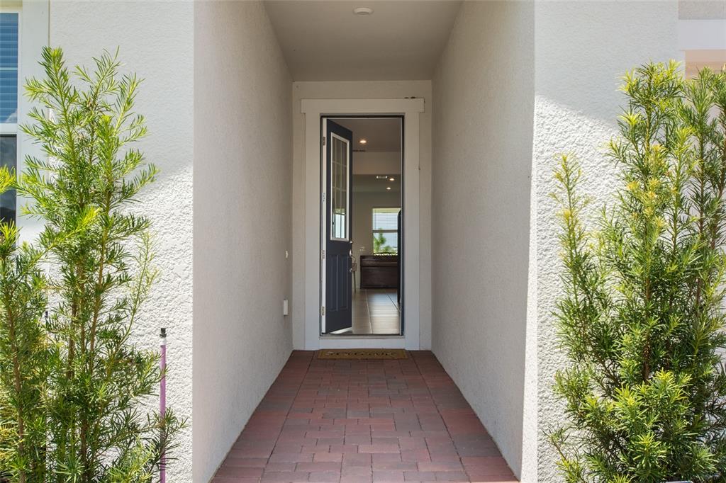 A brick walkway leads to an open front door of a house with two shrubs — 2685 SWEET ACACIA DRIVE, CLERMONT, FL