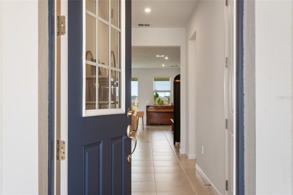 A view through an open dark blue front door into a tiled hallway and living area — 2685 SWEET ACACIA DRIVE, CLERMONT, FL
