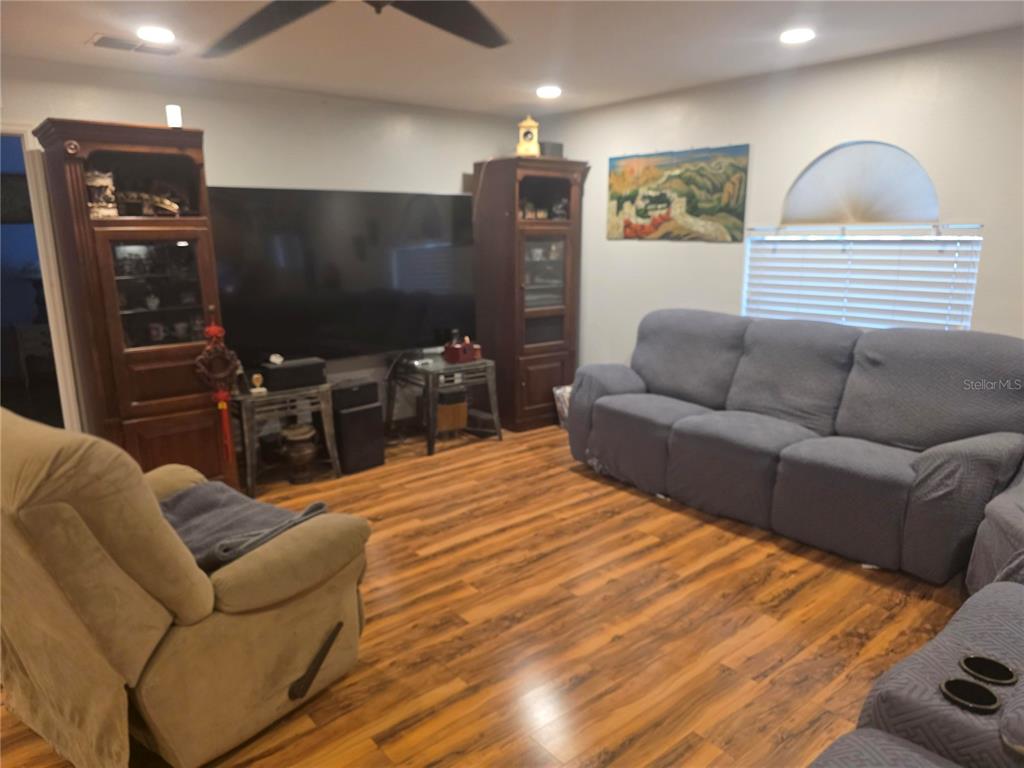 A living room features wood-look flooring, a large television, two wooden cabinets, and gray seating — 959 THOMAS ROAD, EAGLE LAKE, FL