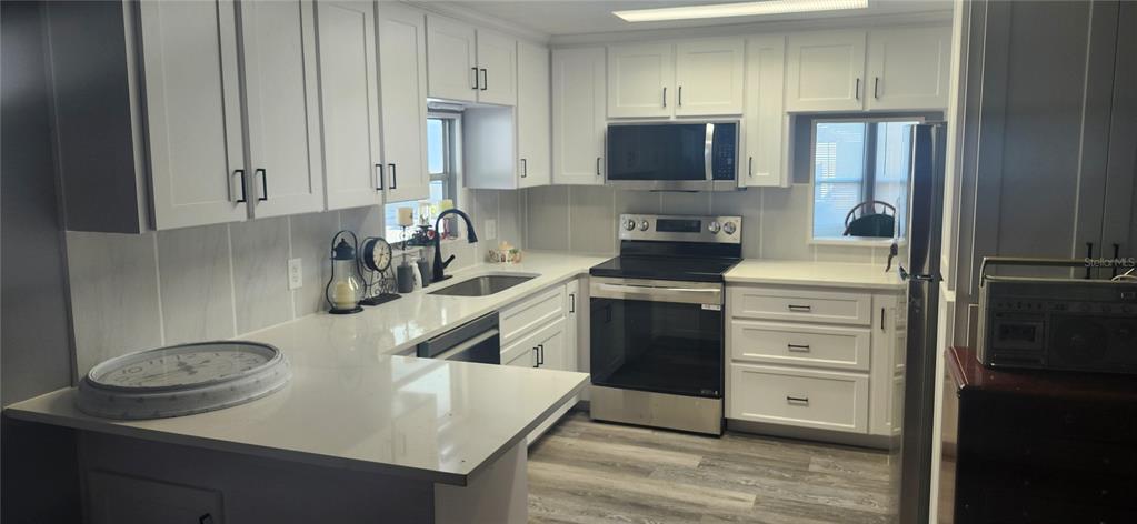 A kitchen features white cabinets, stainless steel appliances, light countertops, and wood-look flooring — 3702 TIKI DRIVE, HOLIDAY, FL