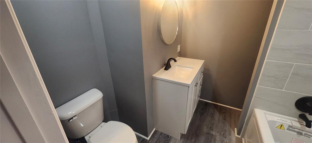 A bathroom features a white vanity, a round mirror, a toilet, and a tiled tub — 3702 TIKI DRIVE, HOLIDAY, FL