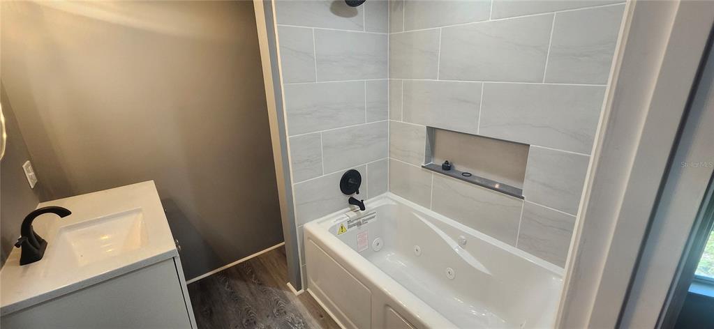 A bathroom features a white vanity with a black faucet and a tiled soaking tub — 3702 TIKI DRIVE, HOLIDAY, FL
