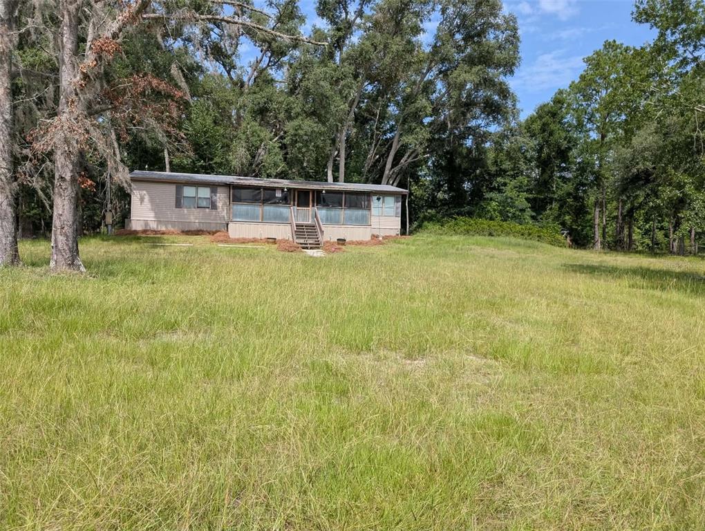 A single-story manufactured home with a screened-in porch sits on a large, grassy lot — 933 NE FIR ST, PINETTA, FL