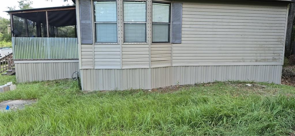 The exterior of a manufactured home features light-colored siding, a screened-in porch, and tall grass — 933 NE FIR ST, PINETTA, FL