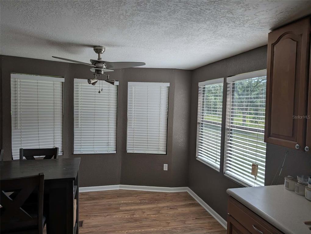 A dining area features wood-look flooring, dark walls, a ceiling fan, and multiple windows — 933 NE FIR ST, PINETTA, FL