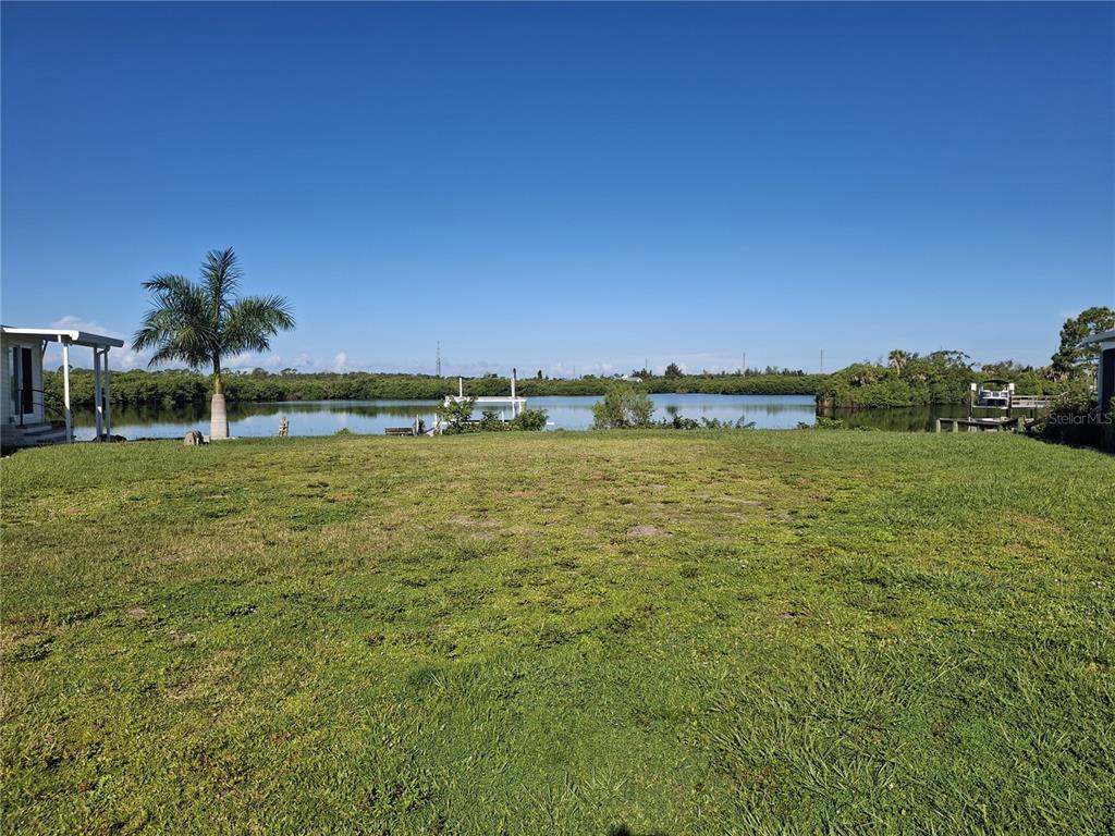 A grassy backyard leads to a waterfront view with a dock and palm tree — 150 MARTINIQUE ROAD UNIT 277, NORTH PORT, FL