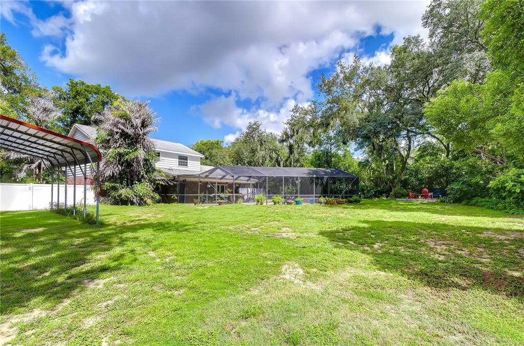 A large backyard features a metal carport, a screened-in pool enclosure, and mature trees — 901 WOODVIEW DRIVE, BRANDON, FL