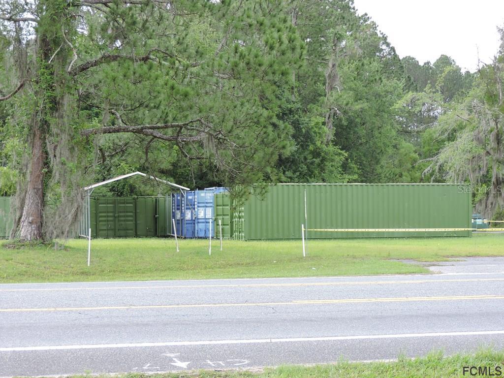 A large green shipping container sits on a grassy lot near a paved road — 725 STATE ROAD, LAKE CITY, FL