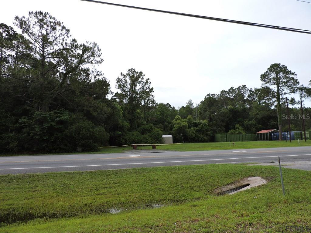 A paved road runs in front of a grassy lot with trees and a small shed — 725 STATE ROAD, LAKE CITY, FL