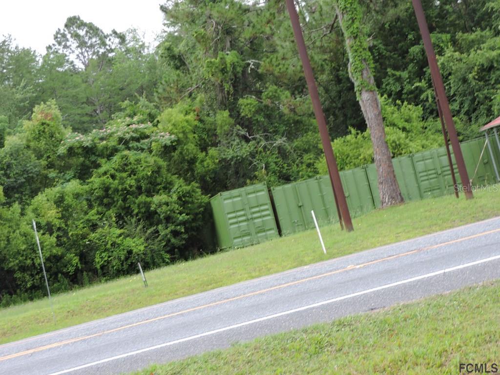 Green shipping containers sit on a grassy lot next to a paved road — 725 STATE ROAD, LAKE CITY, FL