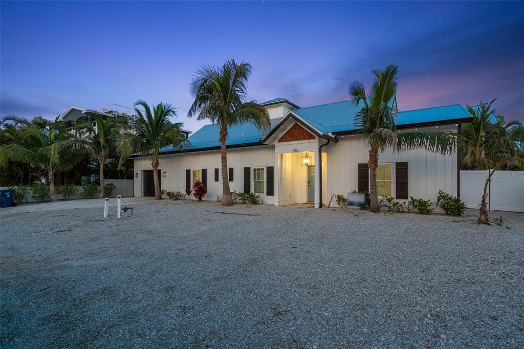 A single-story house with a blue metal roof and white siding sits on a gravel lot — 305 73RD STREET, HOLMES BEACH, FL