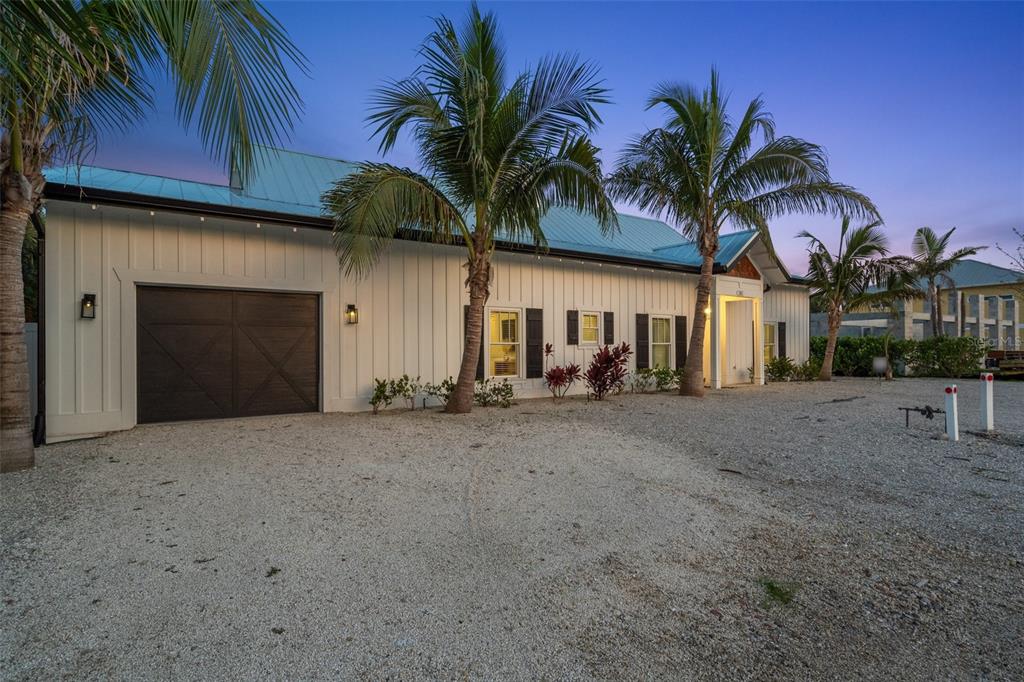 A white farmhouse-style home with a metal roof and gravel driveway at dusk — 305 73RD STREET, HOLMES BEACH, FL