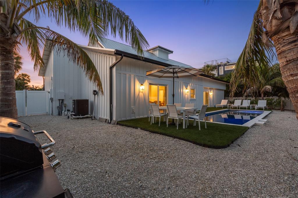 A white farmhouse-style home features a backyard with a swimming pool, patio, and palm trees — 305 73RD STREET, HOLMES BEACH, FL