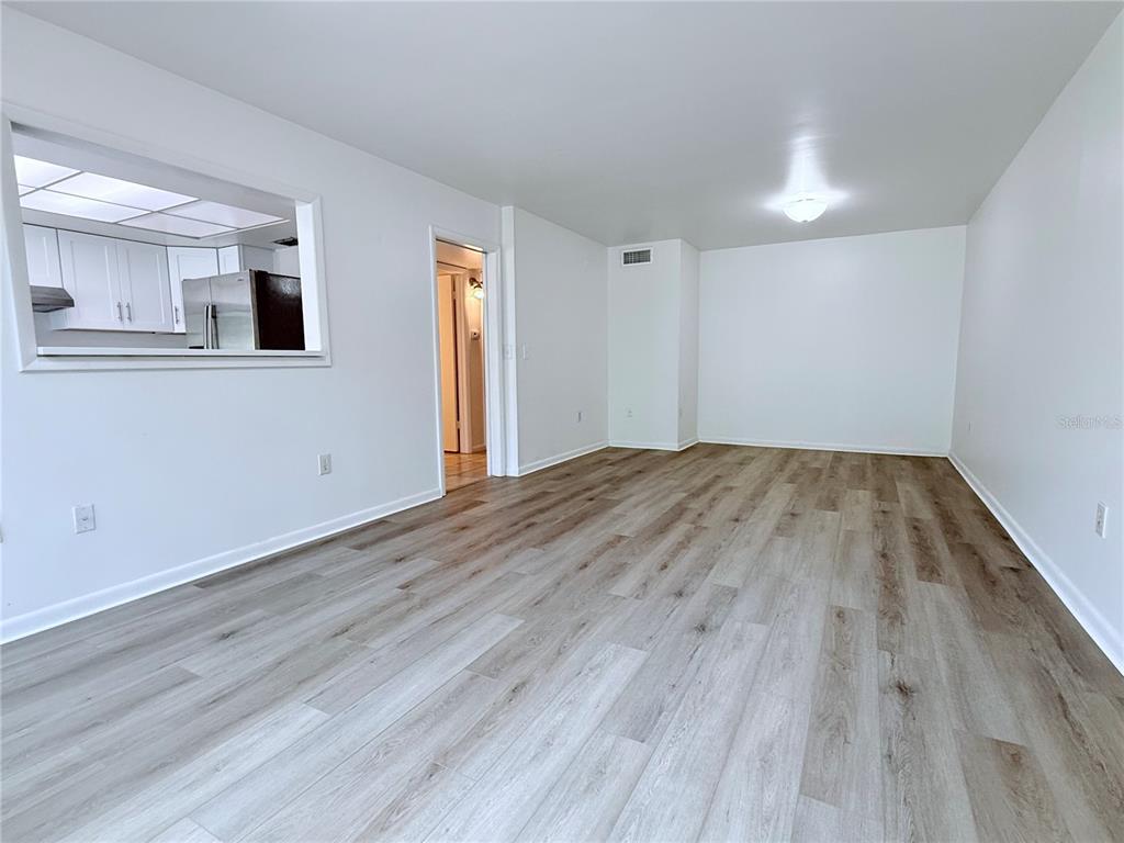 An empty room with light wood-look flooring, white walls, and a pass-through window to the kitchen — 6206 DEWDROP WAY, TEMPLE TERRACE, FL