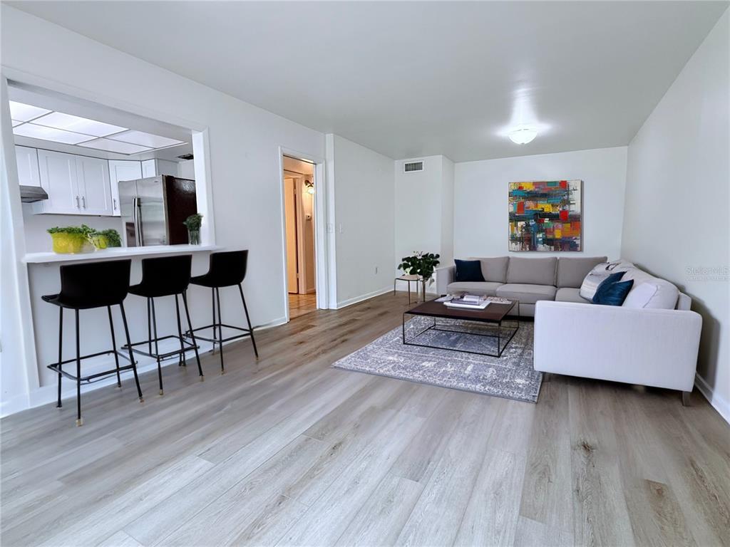 A living room with light wood flooring, a grey sectional sofa, and a kitchen breakfast bar — 6206 DEWDROP WAY, TEMPLE TERRACE, FL