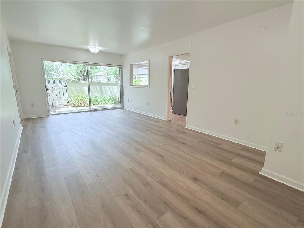 An empty living room features light wood-look flooring, white walls, and a sliding glass door — 6206 DEWDROP WAY, TEMPLE TERRACE, FL