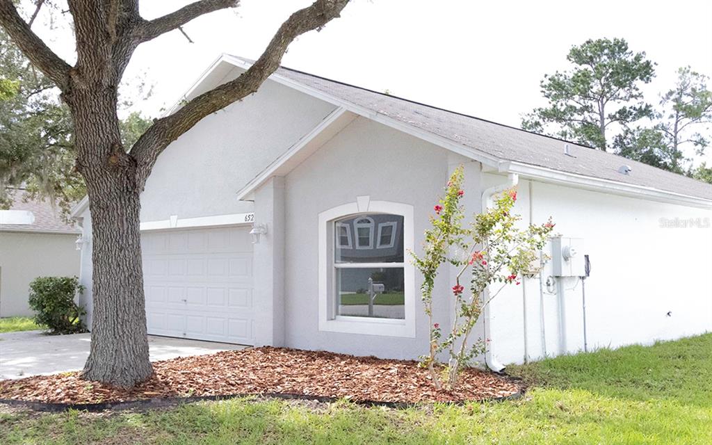 A white stucco exterior wall features a bright red front door and a concrete walkway — 6529 TABOGI TRAIL, WESLEY CHAPEL, FL