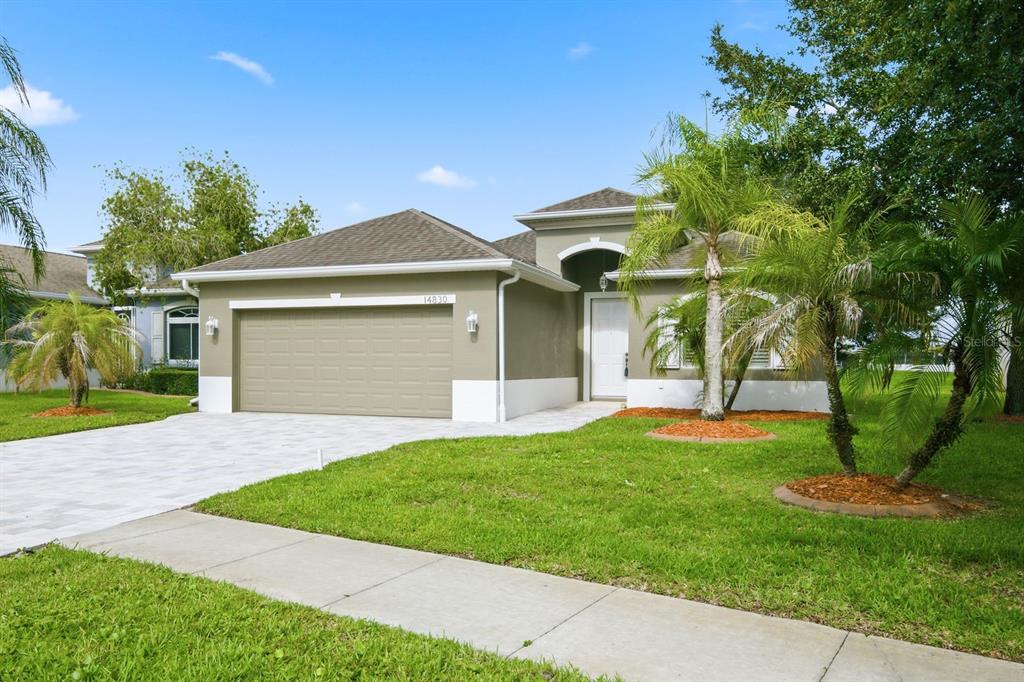 A single-story house with a two-car garage, white trim, and palm trees in the yard — 14830 POTTERTON CIRCLE, HUDSON, FL