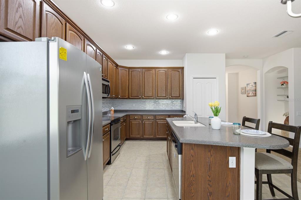 A kitchen with wood cabinets, stainless steel appliances, a gray island, and tile flooring — 14830 POTTERTON CIRCLE, HUDSON, FL