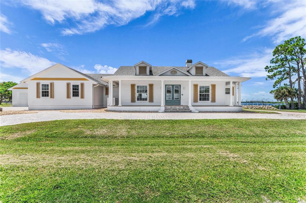 A white single-story house with a wraparound porch and brown shutters sits on a lawn — 12323 LACKAWANNA LANE, PORT CHARLOTTE, FL