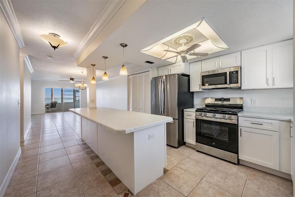 A kitchen with white cabinets, stainless steel appliances, and a large island overlooks a living area — 7 DUNOON PLACE UNIT 102, DUNEDIN, FL