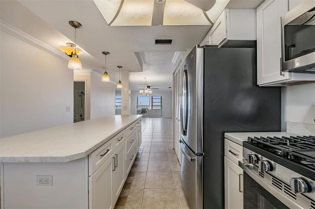 A kitchen with white cabinets, a long countertop, stainless steel appliances, and tile flooring — 7 DUNOON PLACE UNIT 102, DUNEDIN, FL