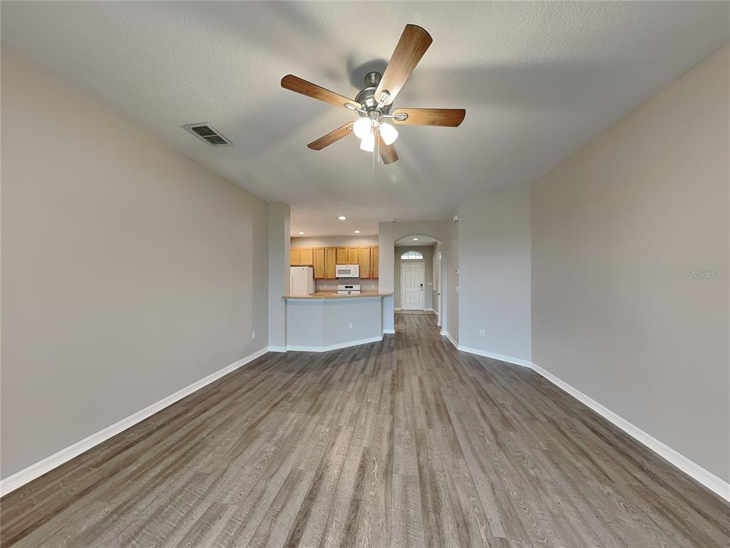 An open living area features wood-look flooring, a ceiling fan, and a view into the kitchen — 221 FERN GULLEY DRIVE, SEFFNER, FL