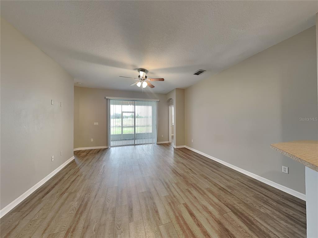 An empty living room features wood-look flooring, a ceiling fan, and sliding glass doors — 221 FERN GULLEY DRIVE, SEFFNER, FL