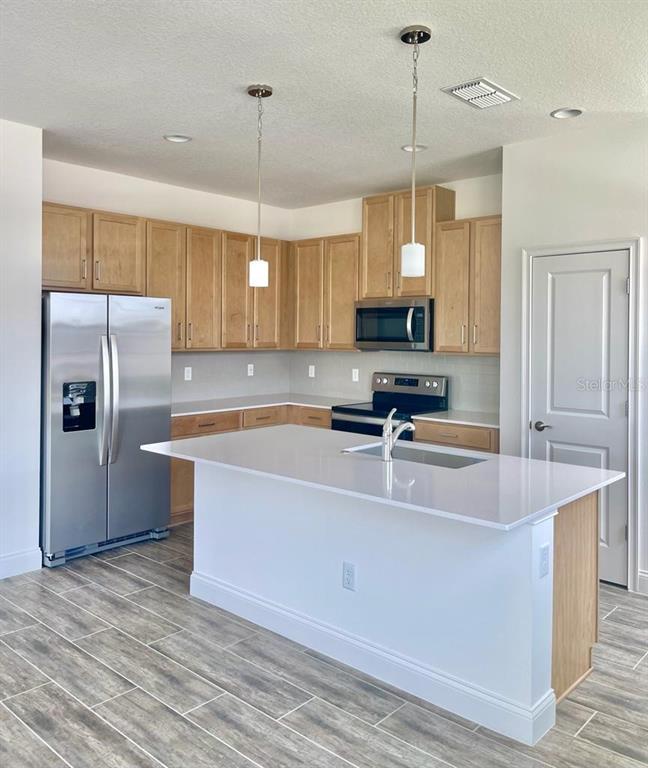 A kitchen features light wood cabinets, stainless steel appliances, a white island, and gray flooring — 3032 CRISPIN CIRCLE, ST CLOUD, FL