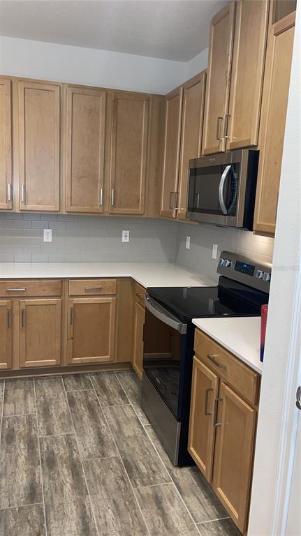 A kitchen features light wood cabinets, white countertops, a subway tile backsplash, and stainless appliances — 3032 CRISPIN CIRCLE, ST CLOUD, FL