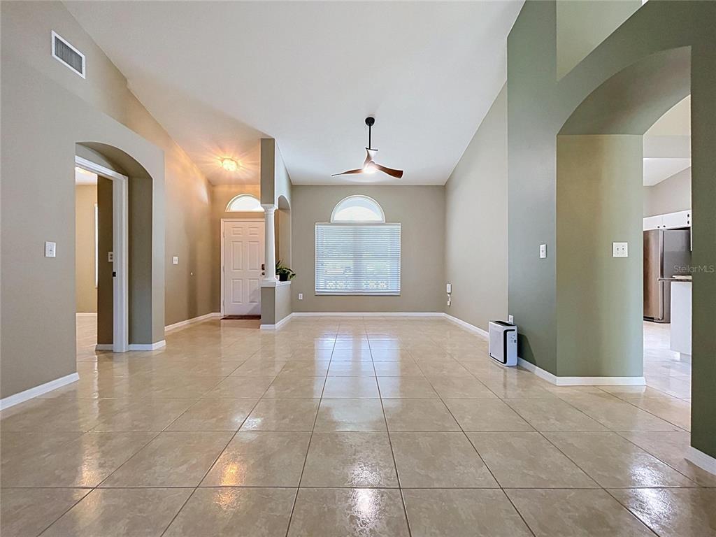 A spacious living room features vaulted ceilings, tile flooring, and a large arched window — 4209 AMBER RIDGE LANE, VALRICO, FL