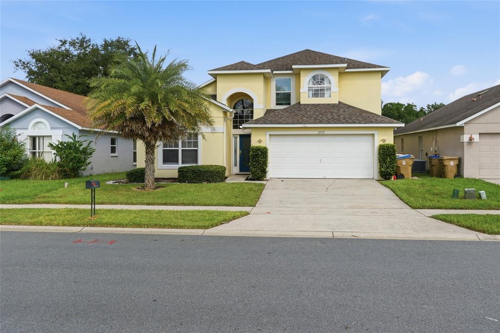 A two-story yellow house with a two-car garage and a palm tree in the yard — 2915 BLOOMING ALAMANDA LOOP, KISSIMMEE, FL
