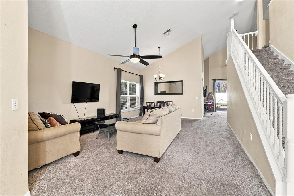A living room with beige carpet, a vaulted ceiling, a ceiling fan, and a staircase — 2915 BLOOMING ALAMANDA LOOP, KISSIMMEE, FL