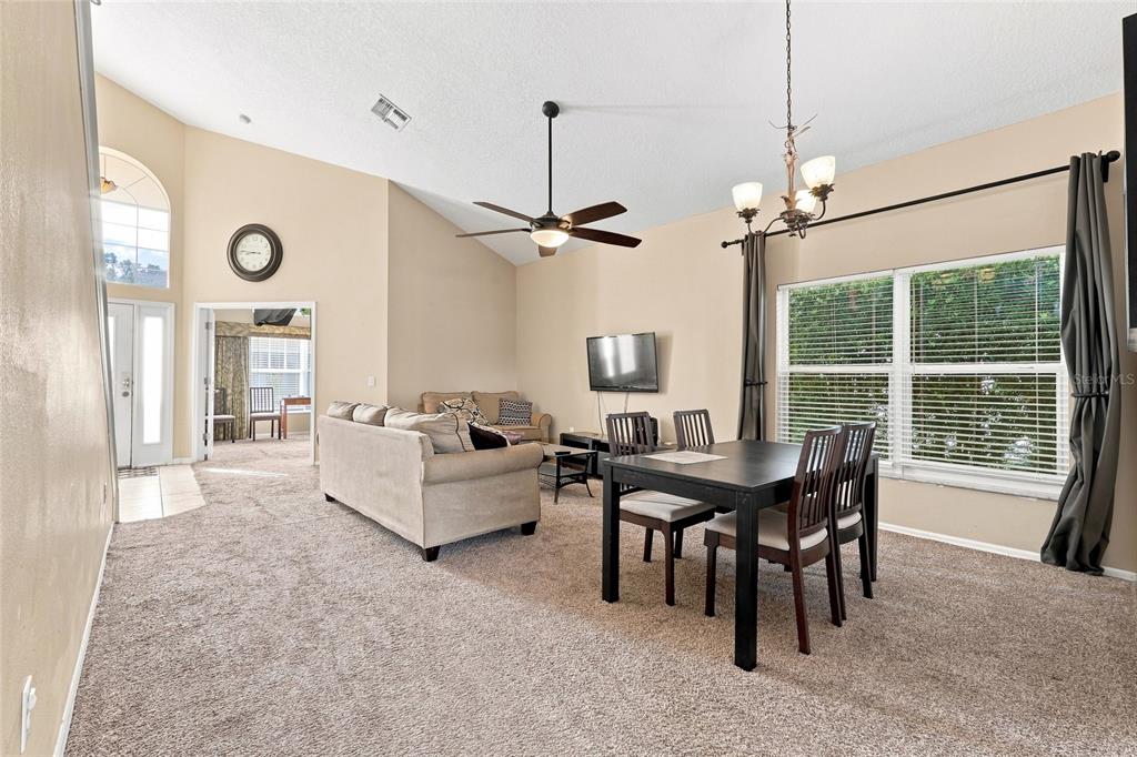 A living and dining area with carpeted floors, a ceiling fan, and large windows — 2915 BLOOMING ALAMANDA LOOP, KISSIMMEE, FL