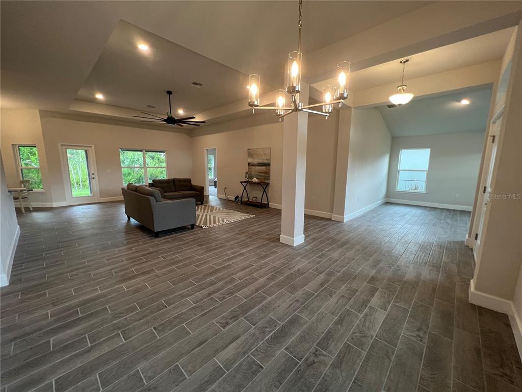 An open-concept living area features wood-look tile flooring, a tray ceiling, and a modern chandelier — 27430 DEEP CREEK BOULEVARD, PUNTA GORDA, FL