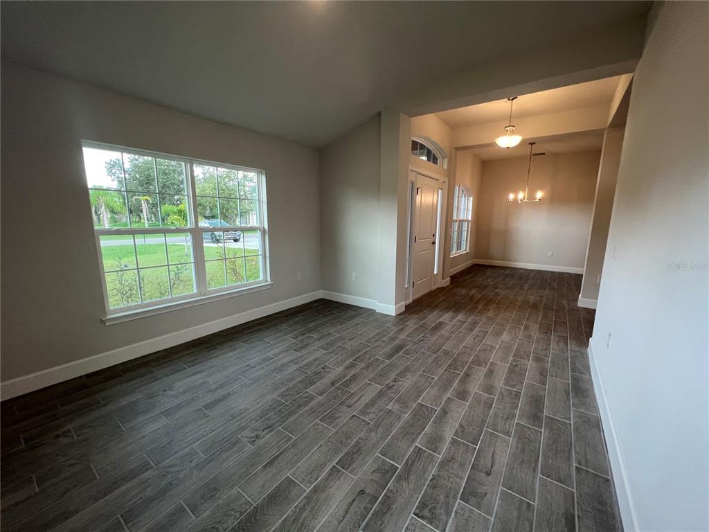 An empty room with gray wood-look tile flooring and a view into a dining area — 27430 DEEP CREEK BOULEVARD, PUNTA GORDA, FL