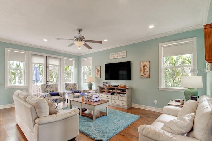 A living room features light blue walls, white sofas, a television, and a blue area rug — 4808 GULF DRIVE UNIT B, HOLMES BEACH, FL