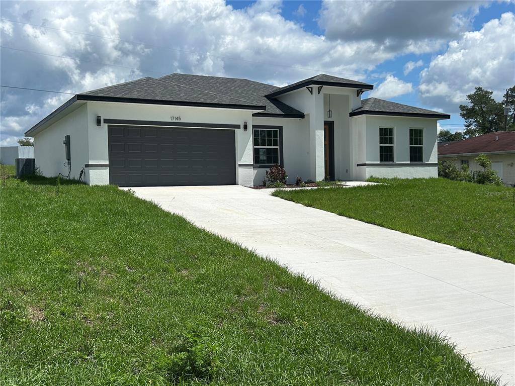 A modern single-story house with a white stucco exterior, dark roof, and a concrete driveway — 17145 SW 44TH CIRCLE, OCALA, FL