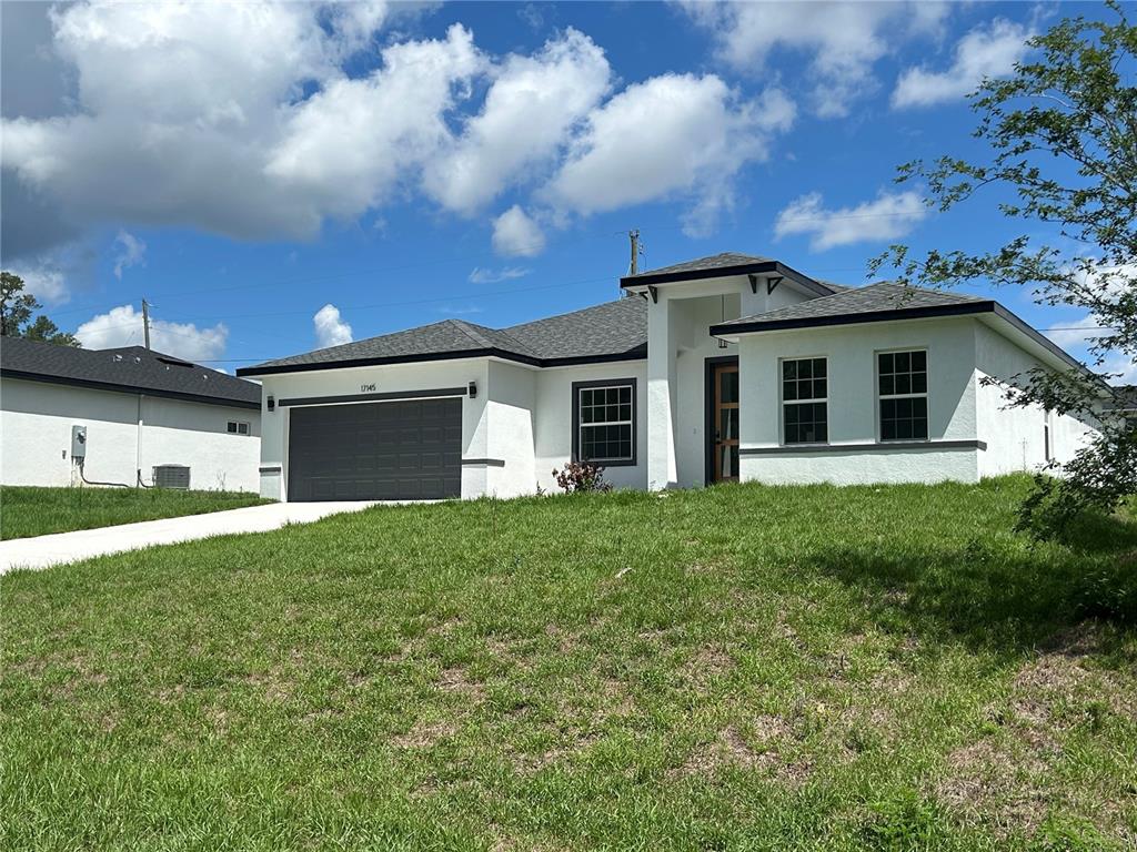 A single-story white house with a dark gray garage door and a shingled roof — 17145 SW 44TH CIRCLE, OCALA, FL